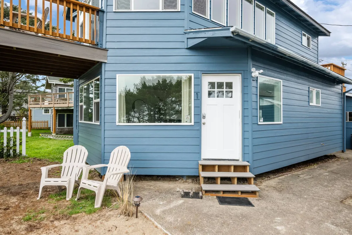 This inviting exterior shot highlights the bright blue facade of the house, a white front door, and two Adirondack chairs placed perfectly for relaxing and enjoying the view. The scene suggests the ease of stepping right outside for a morning coffee or an evening spent watching sunsets, aligning with the section's emphasis on romantic and spontaneous beachside moments.