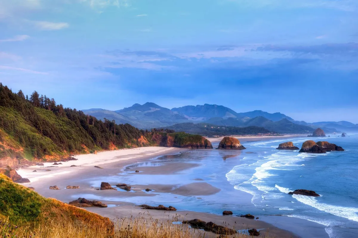 A breathtaking view of the nearby coastline, with the sandy beach stretching toward distant mountains and the iconic rocky outcrops visible offshore. Gentle waves lap the shore, capturing the tranquil, scenic beauty referenced in the content.