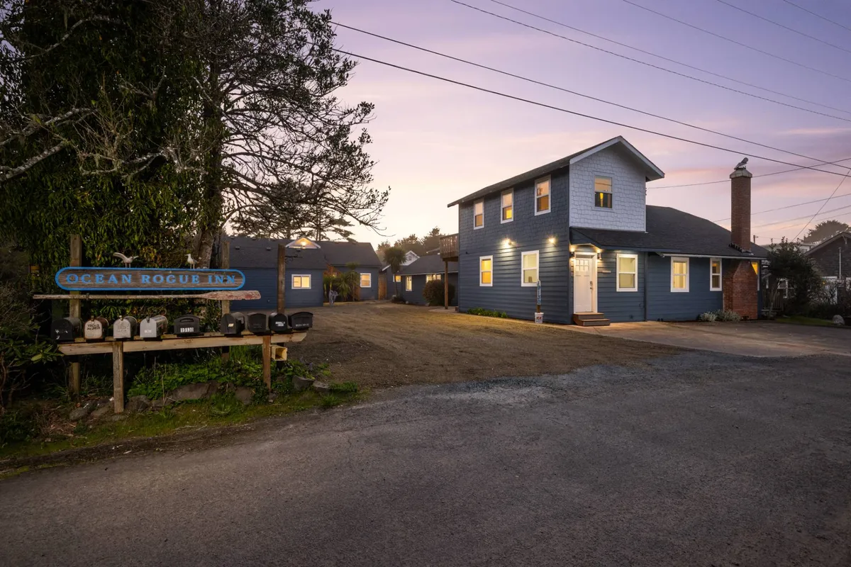 A tranquil scene featuring the Ocean Rogue Inn's sign, the welcoming facade of the building, and mature trees providing shade and privacy. The inviting front porch suggests a sense of arrival and reassurance, while the surrounding greenery enhances the feeling of peaceful seclusion.